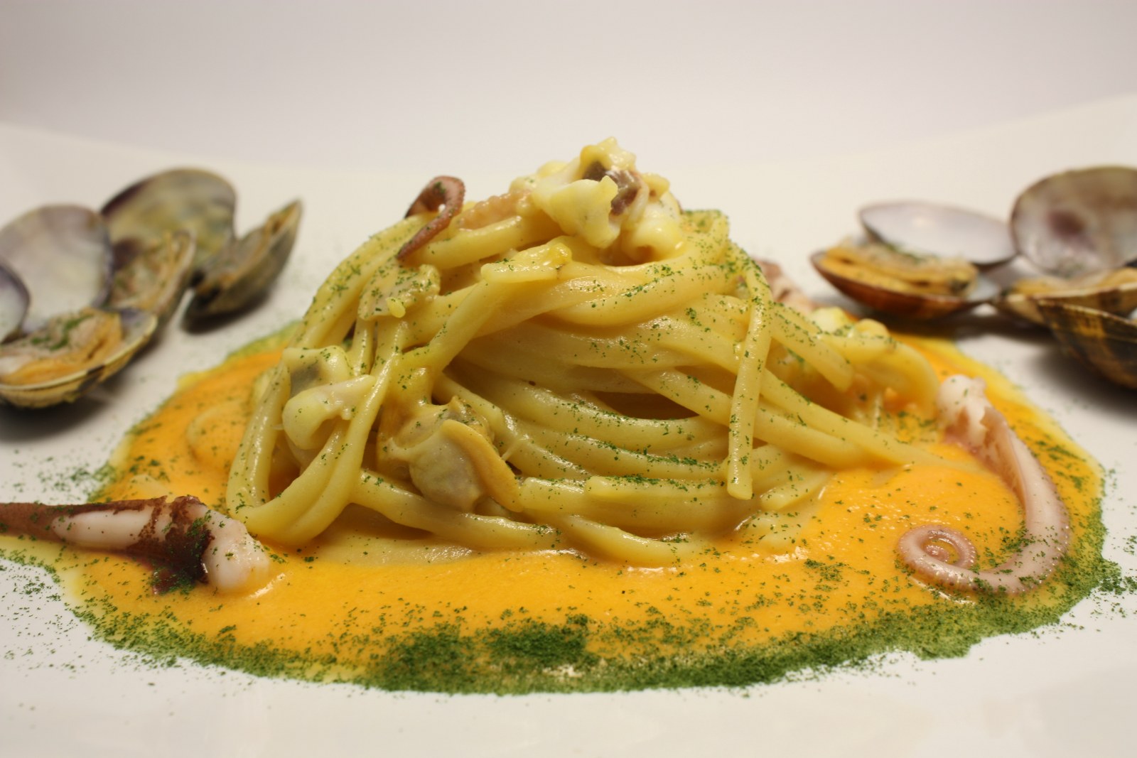Linguine con crema di patate colorata allo zafferano, polipetti veraci e vongole su vellutata di zucca, imbrattate con polvere di prezzemolo